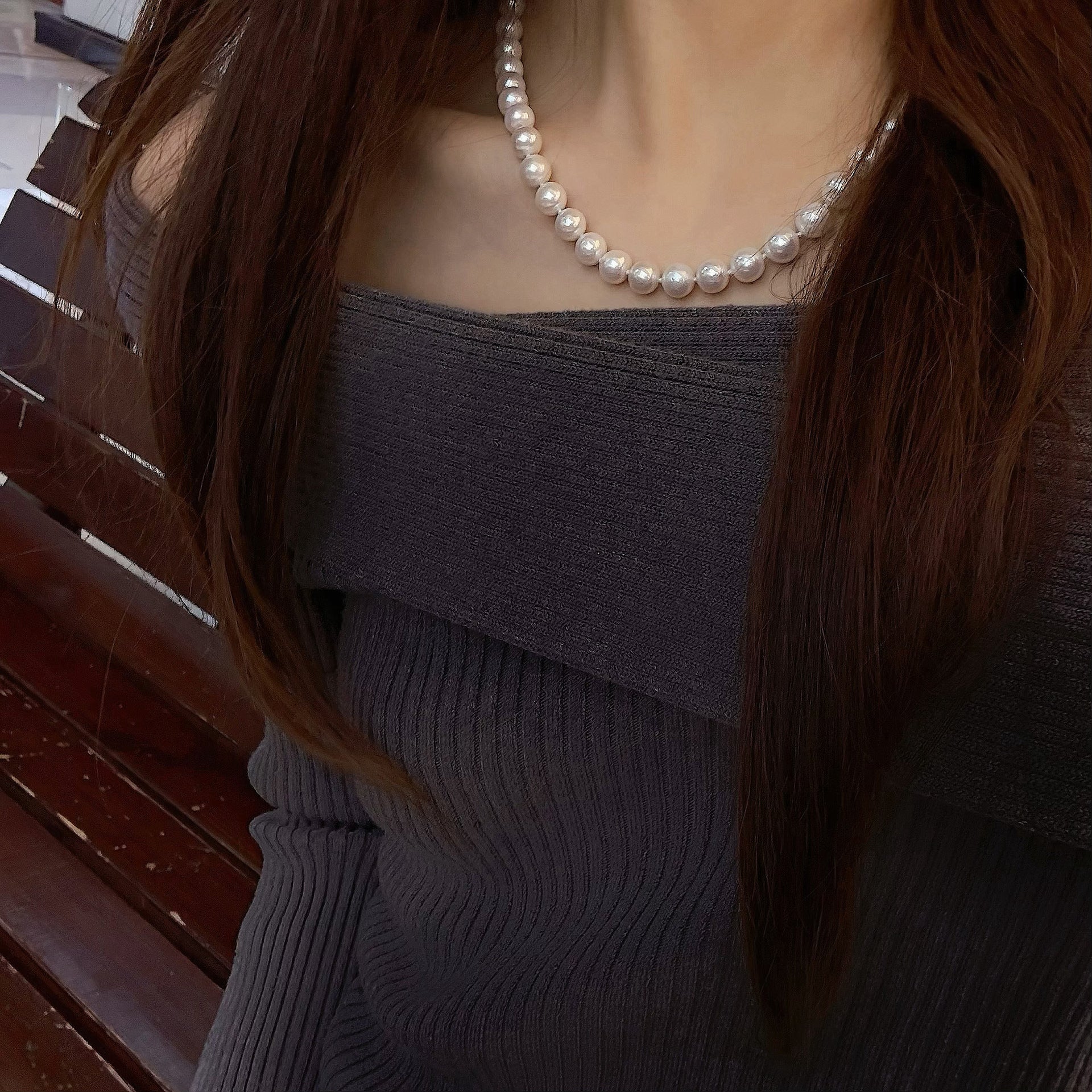 model wearing a dark gray off-shoulder top with a pearl necklace