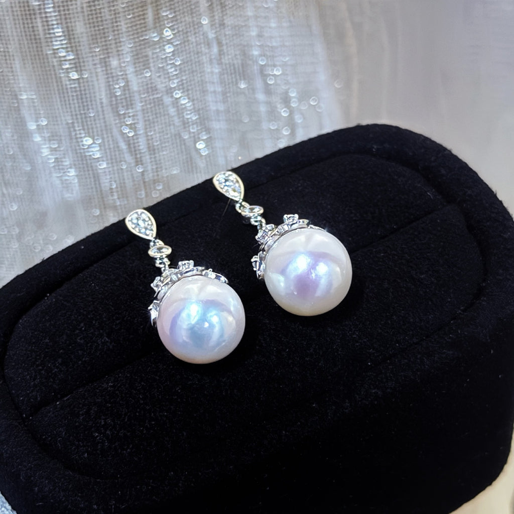 Pearl earrings with silver fixtures on a black cushion against a textured black background