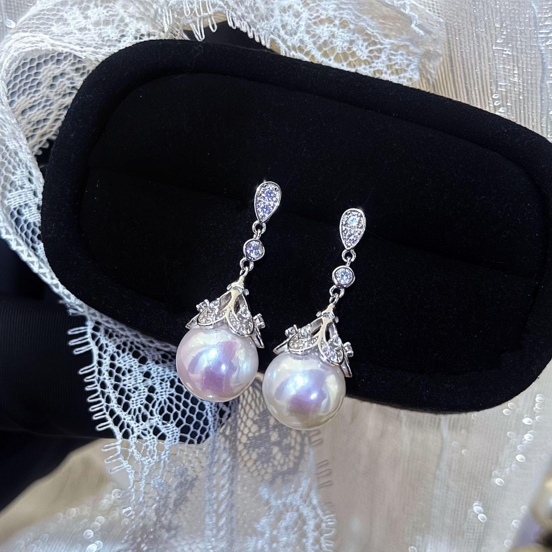 Pearl earrings with silver accents on a black cushion against a lace background